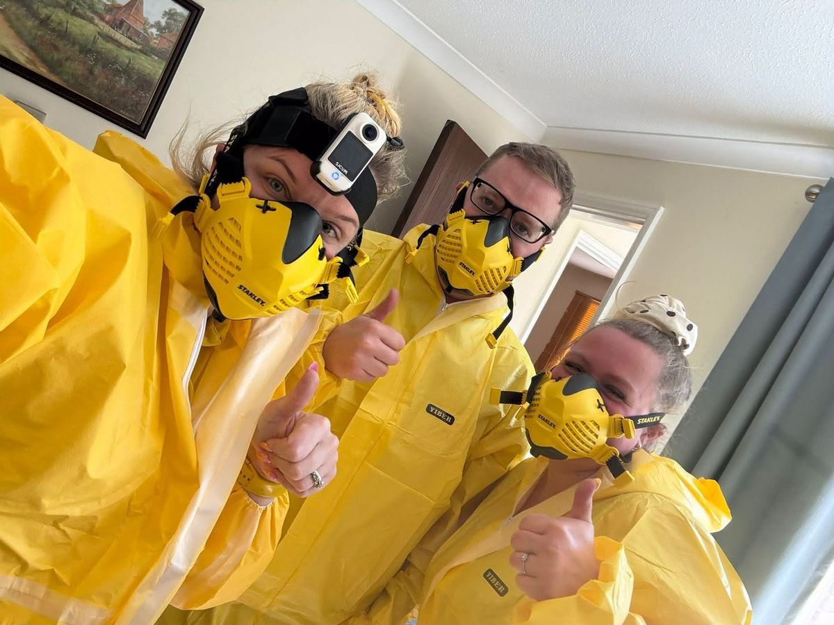 Three members of the Simply Sorted team in yellow protective suits and respirator masks, giving a thumbs up